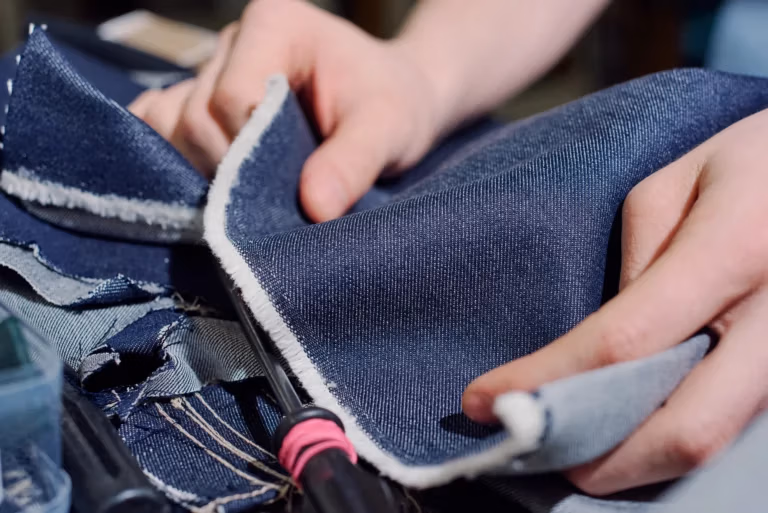 Zwei Hände umgreifen ein Jeansstoff und überprüfen diesen auf Qualität.